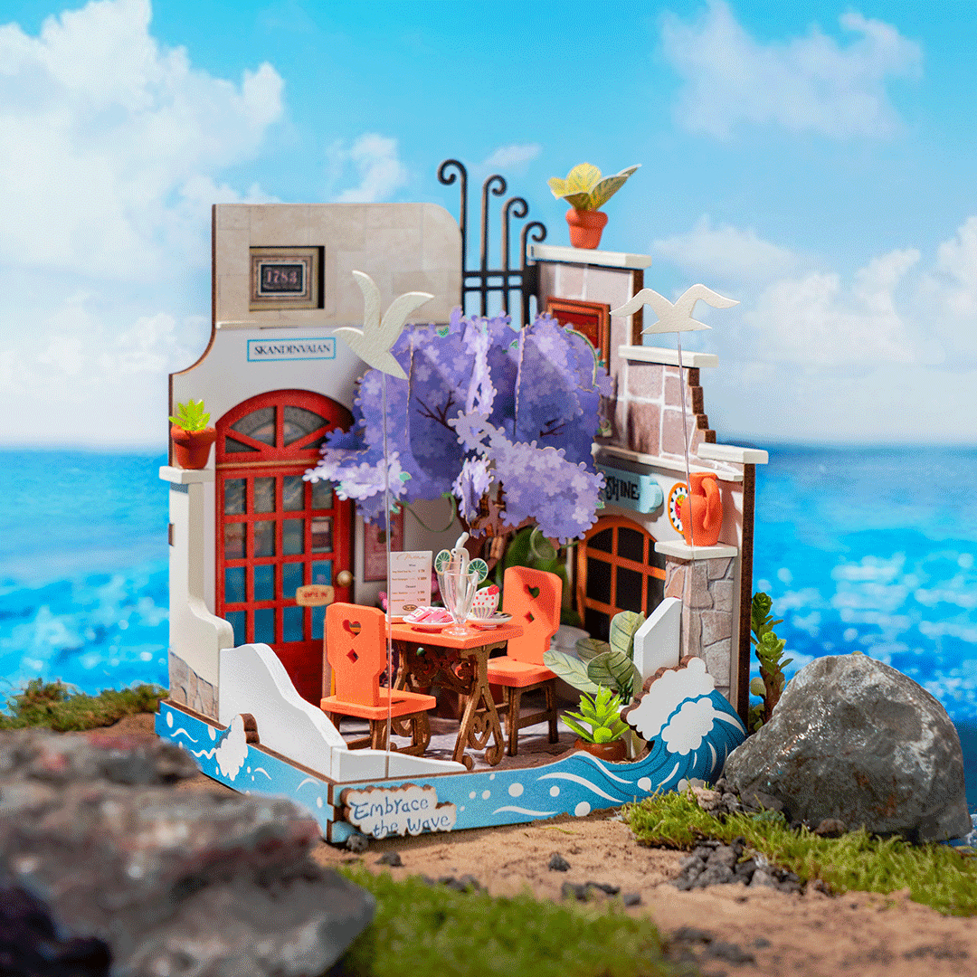 Un café miniature en bord de mer avec chaises orange, arbre violet et fond marin bleu.