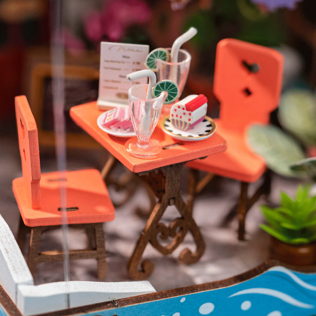 Table de café miniature avec chaises orange, boissons, parts de gâteau et menu.