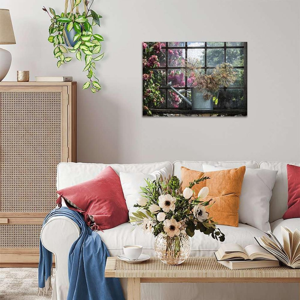 Un salon avec un canapé blanc, une table basse et un tableau d'arrosoir près d'une fenêtre.