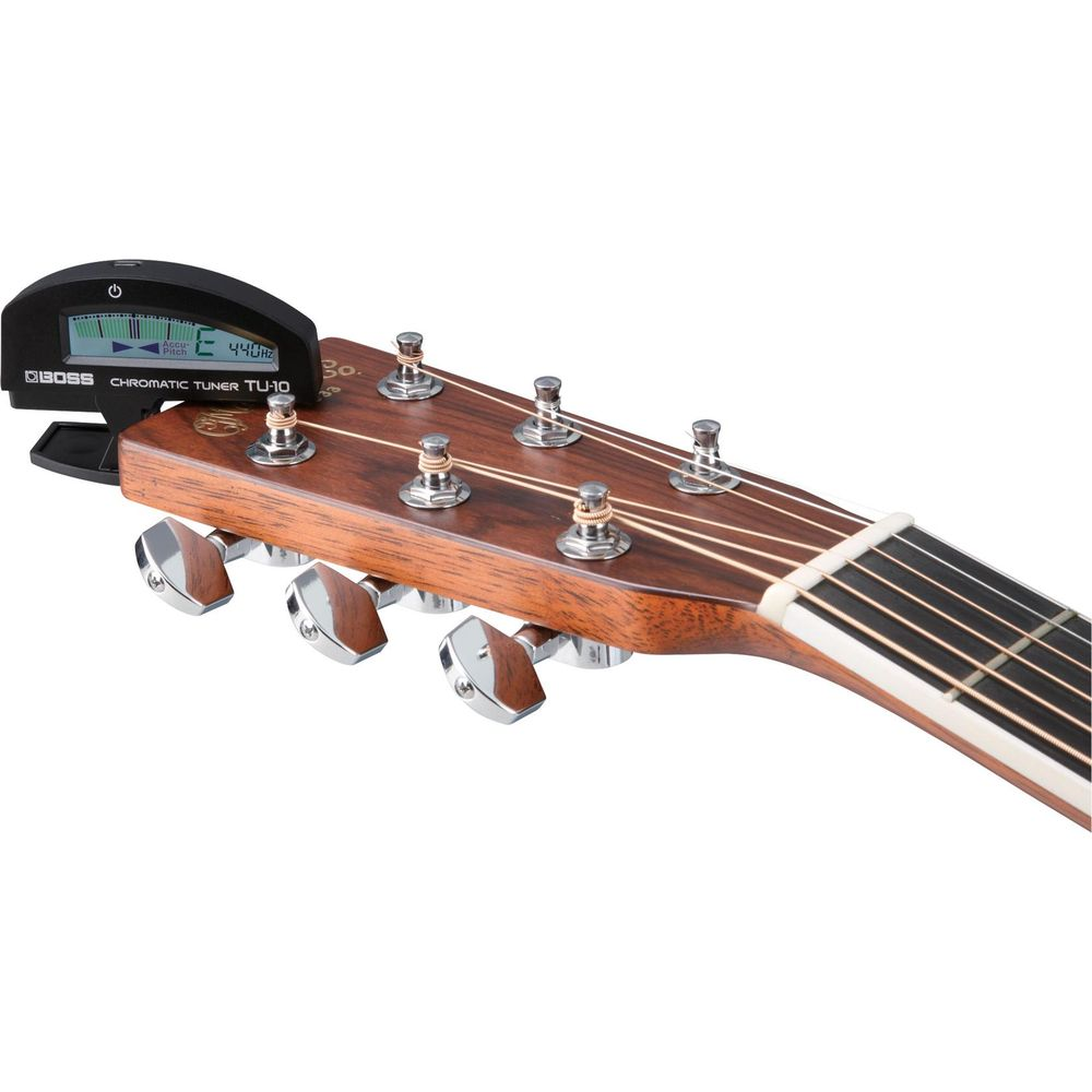 Ein schwarzes Gitarrenstimmgerät wird auf die Kopfplatte einer braunen Akustikgitarre geklemmt.