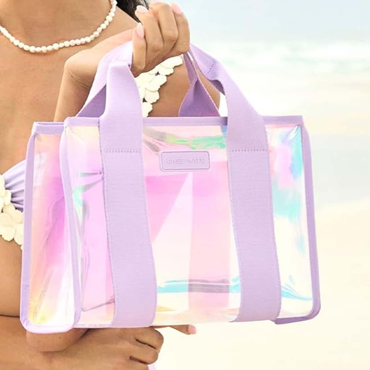 Borsa trasparente con manici viola tenuta da una donna in spiaggia.