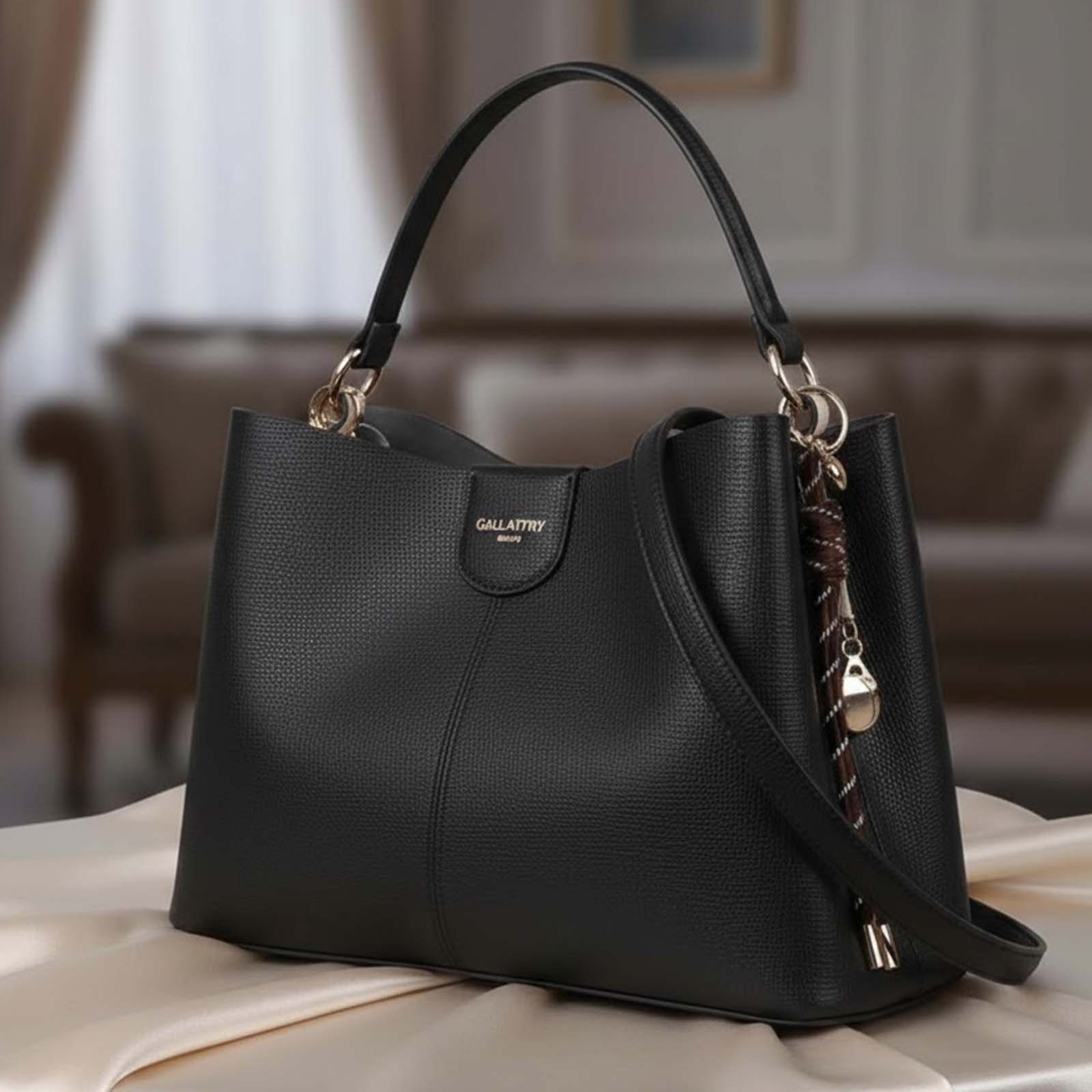 Bolso negro de cuero con asas y amuleto sobre tela clara.