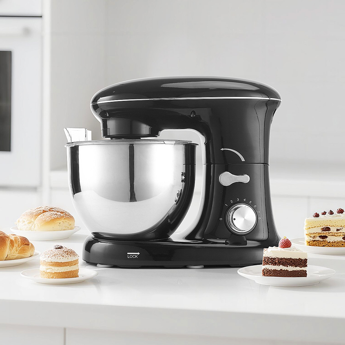 Ein schwarzer Küchenmixer mit Edelstahlschüssel steht auf einer Arbeitsplatte, umgeben von Gebäck.