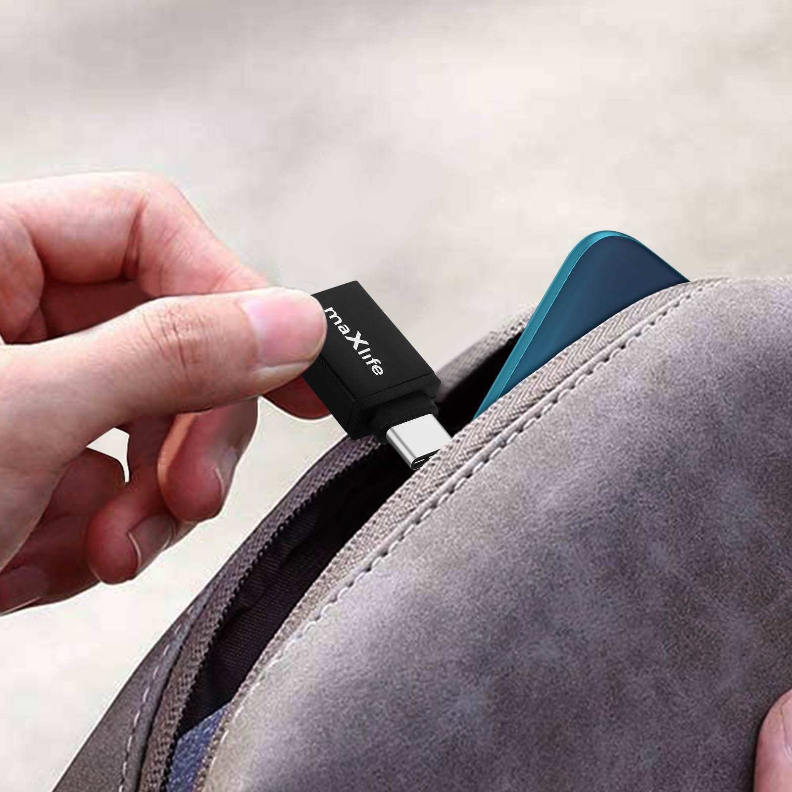 Una mano tiene un adattatore USB-C nero con etichetta 'maXlife' vicino a una borsa.