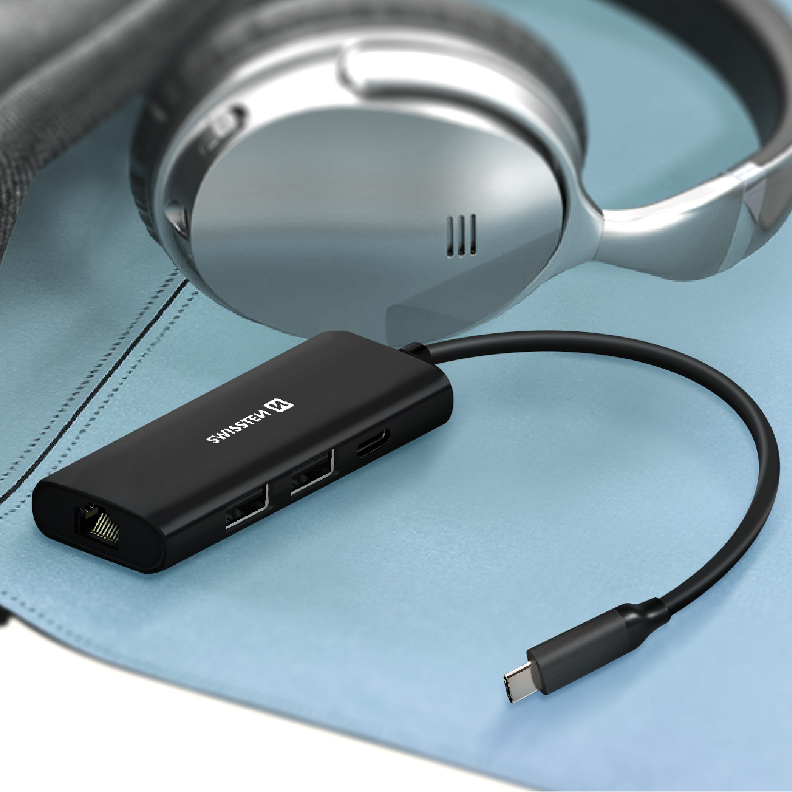 Hub USB-C nero con porte, accanto a cuffie argentate su superficie blu.
