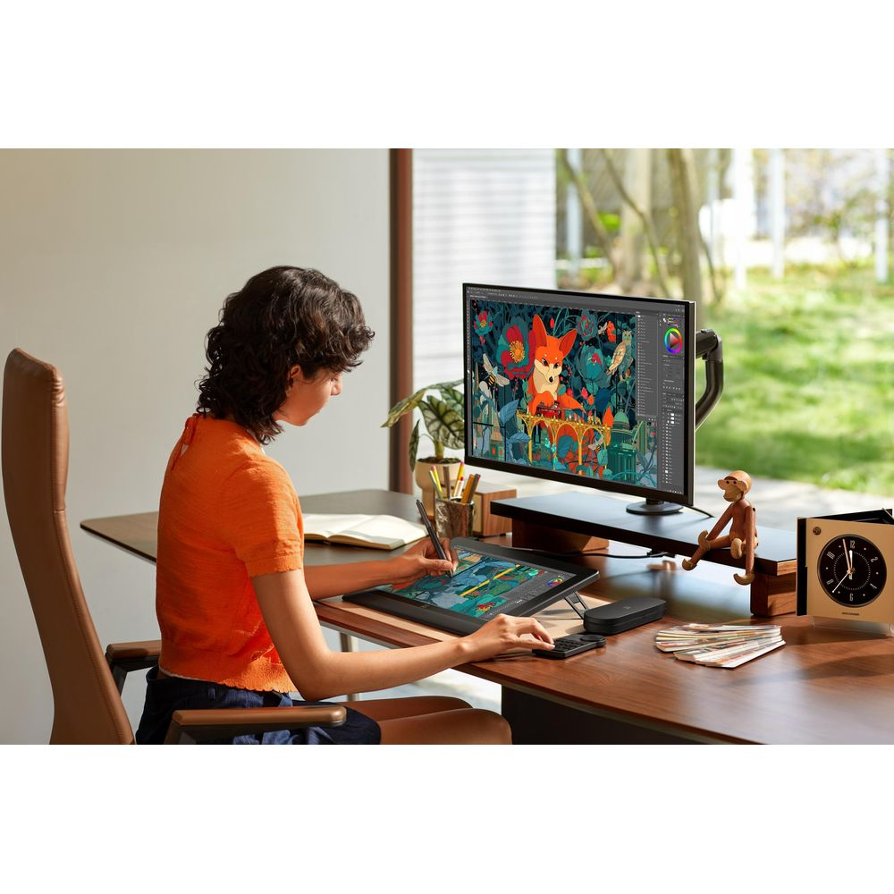 Eine Person in einem orangefarbenen Hemd zeichnet auf einem Tablet an einem Schreibtisch mit einem großen Monitor, der digitale Kunst zeigt.