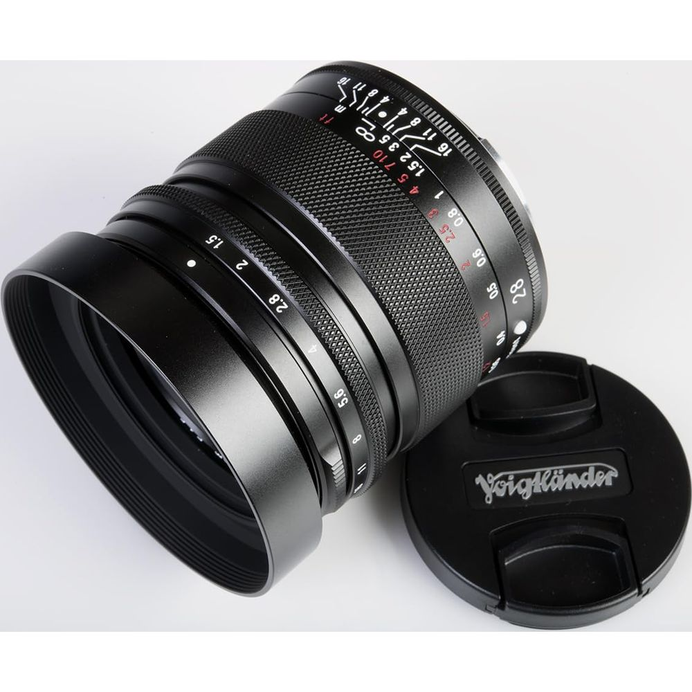 A black camera lens with a Voigtländer cap rests on a white background.
