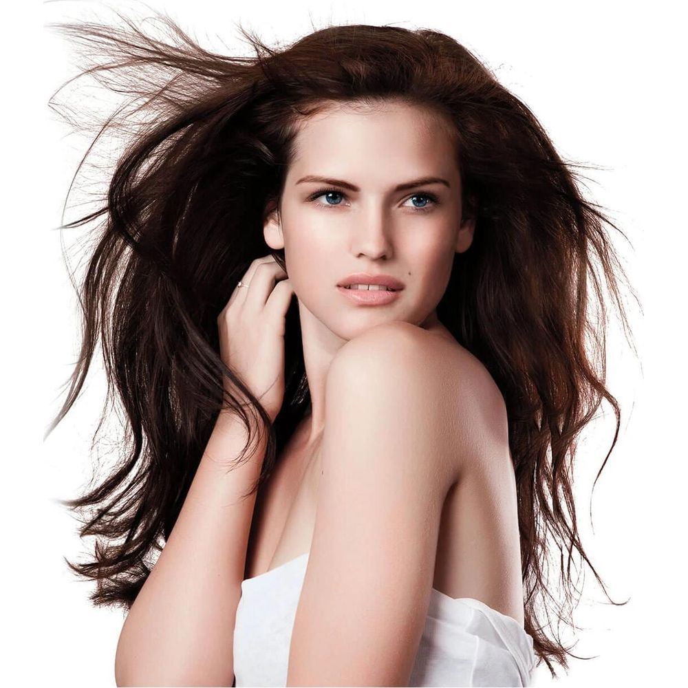 Ein Model mit langen braunen Haaren und blauen Augen, das ein weißes Oberteil trägt.