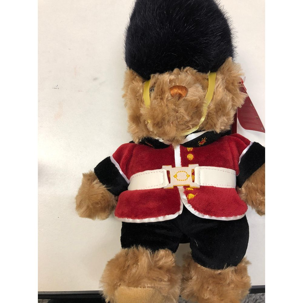 Un ours en peluche portant un uniforme rouge, un pantalon noir et un chapeau noir.