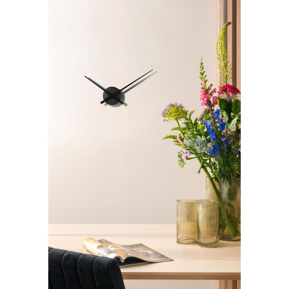 Un orologio nero minimalista su una parete color crema sopra un tavolo con fiori e una rivista.