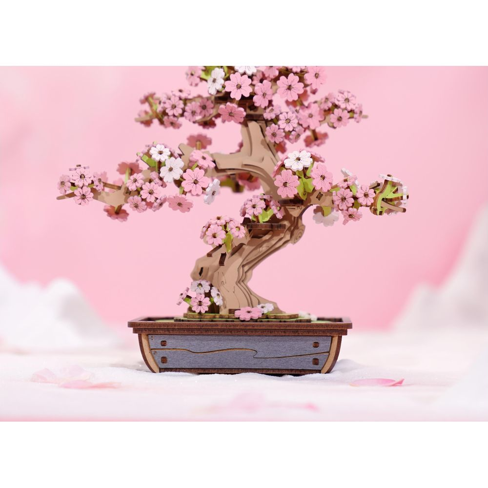 Un bonsai di legno con fiori rosa e bianchi in un vaso grigio.