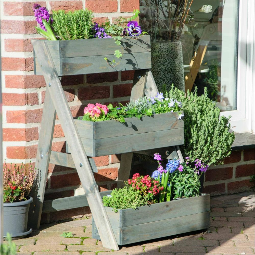 Una fioriera in legno a più livelli con fiori e verde contro un muro di mattoni.