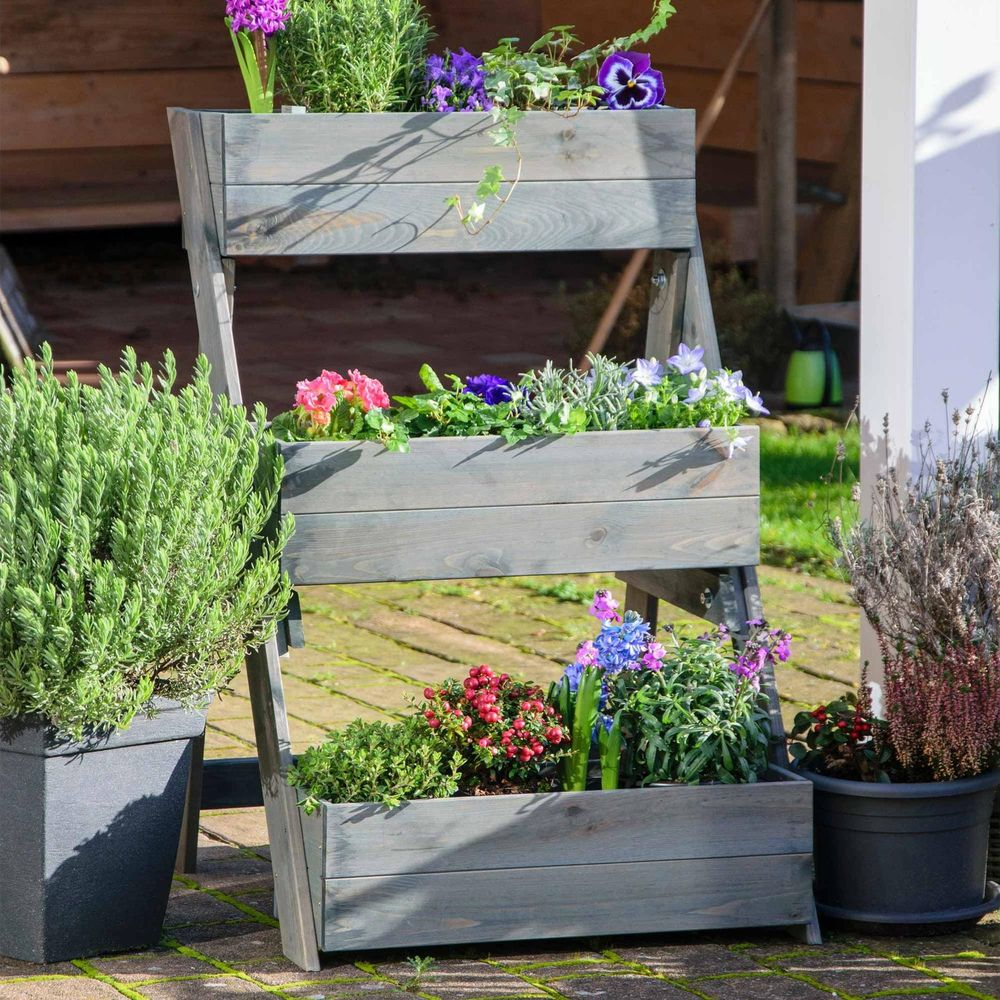 Un fioriera a gradoni in legno grigio con fiori colorati e fogliame verde.