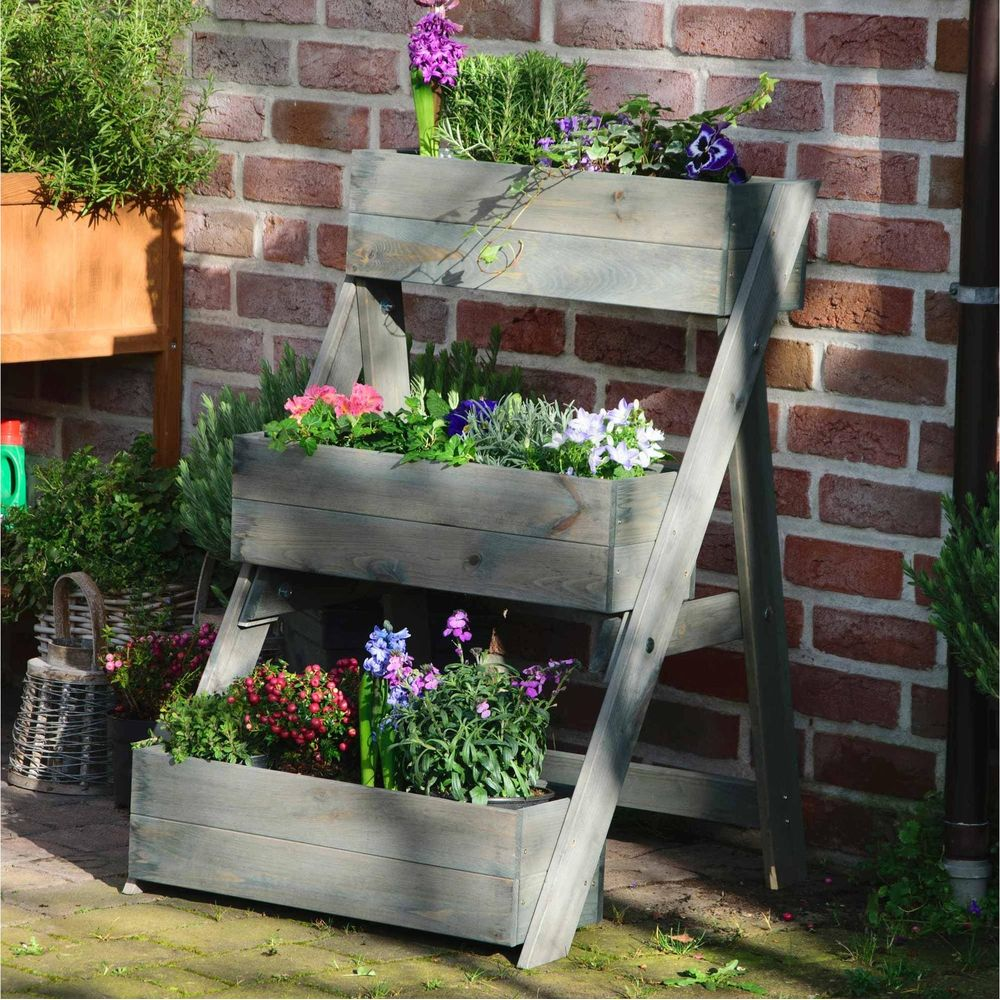 Fioriere in legno a più livelli con fiori colorati e piante verdi contro un muro di mattoni.