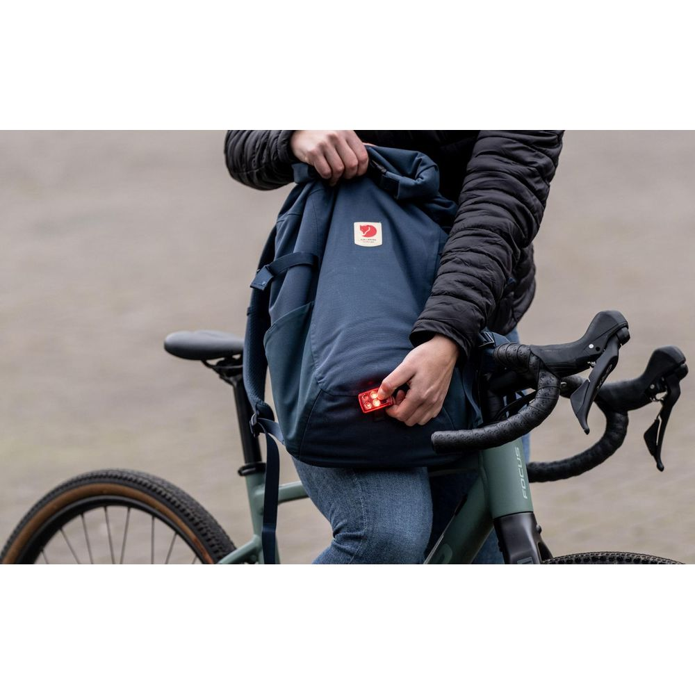 Eine Person befestigt eine rote Fahrradlampe an einem dunkelblauen Rucksack.