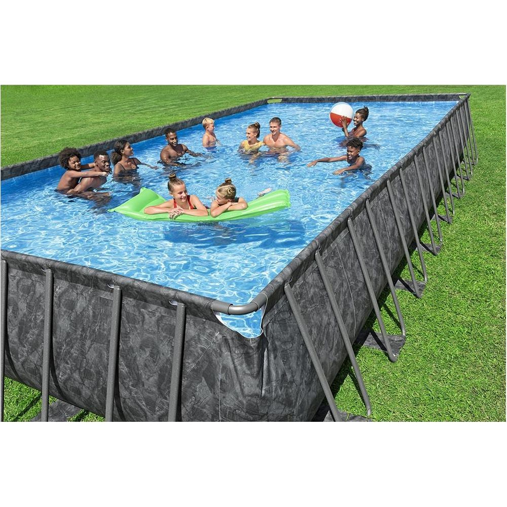 Des gens barbotent dans une piscine rectangulaire extérieure sur une pelouse.