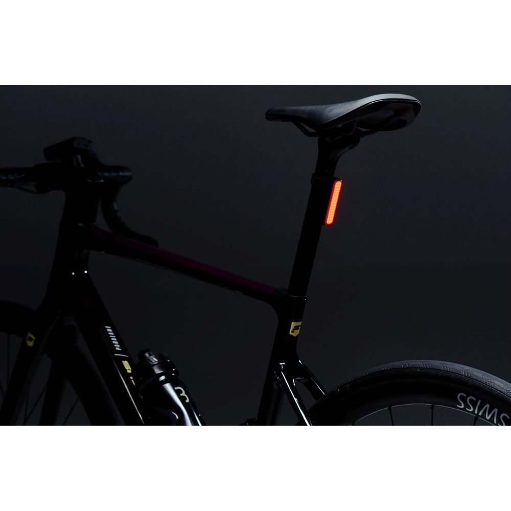 Ein schwarzes Fahrrad mit rotem Rücklicht am Sitzrohr vor dunklem Hintergrund.