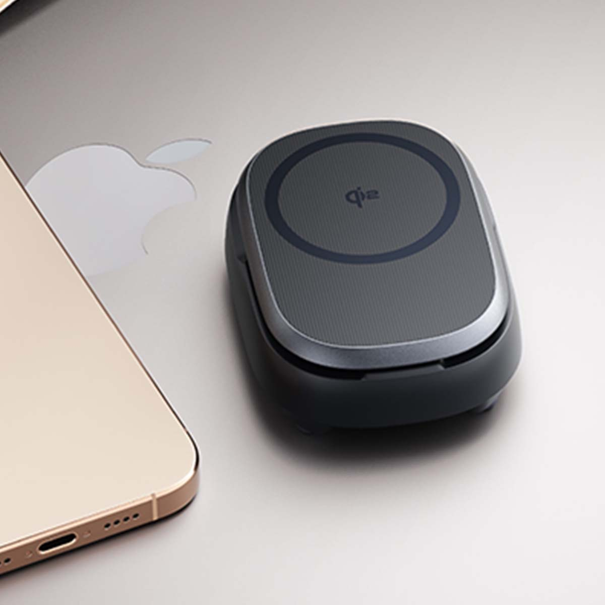 Un iPhone dorato e un caricabatterie wireless Qi nero poggiano su una superficie argentata.
