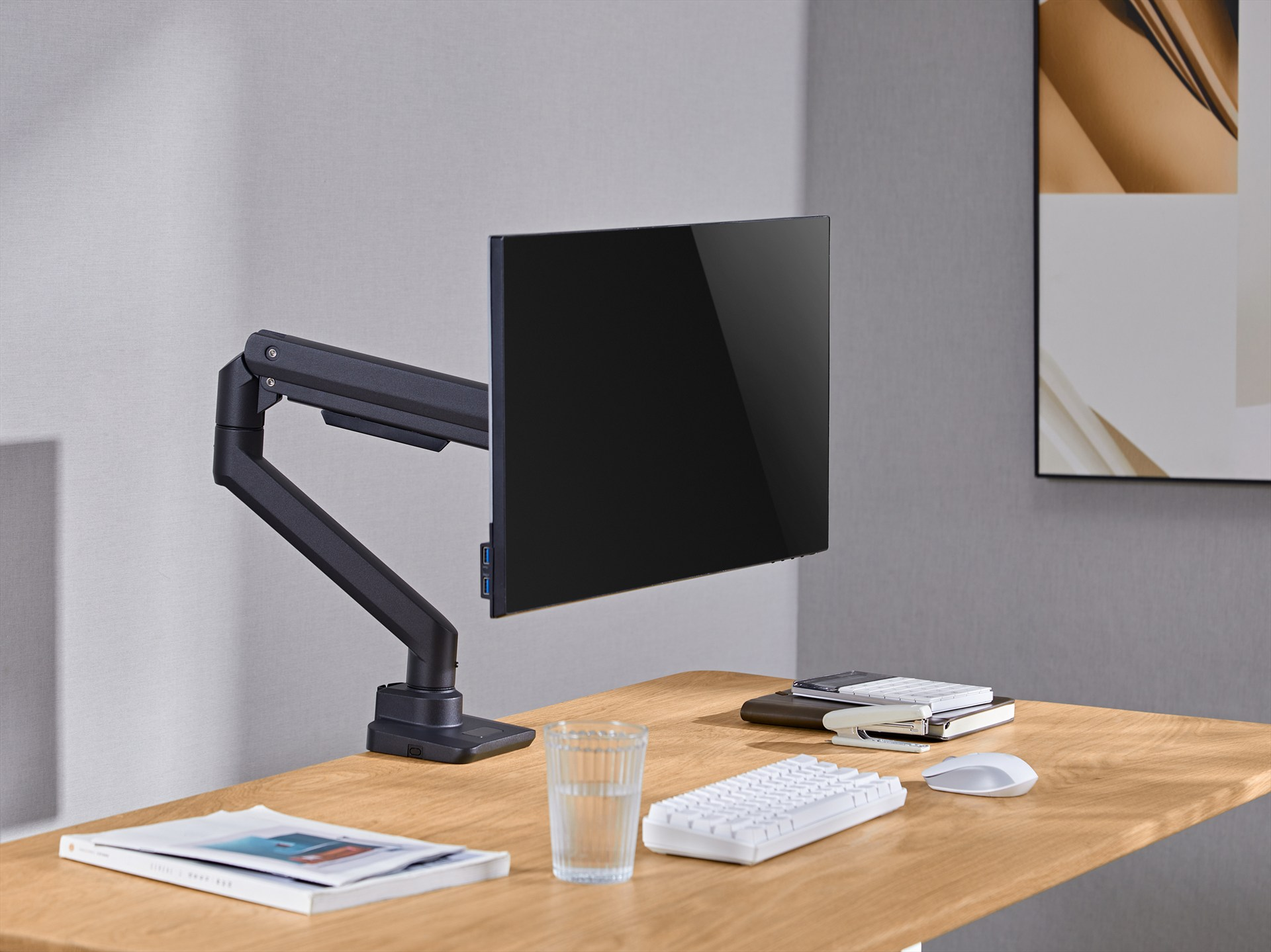 Een zwarte monitor aan een verstelbare arm staat op een houten bureau met toetsenbord en muis.