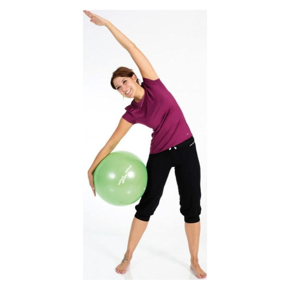 Eine Frau in lila Shirt und schwarzen Hosen dehnt sich mit einem grünen Ball.