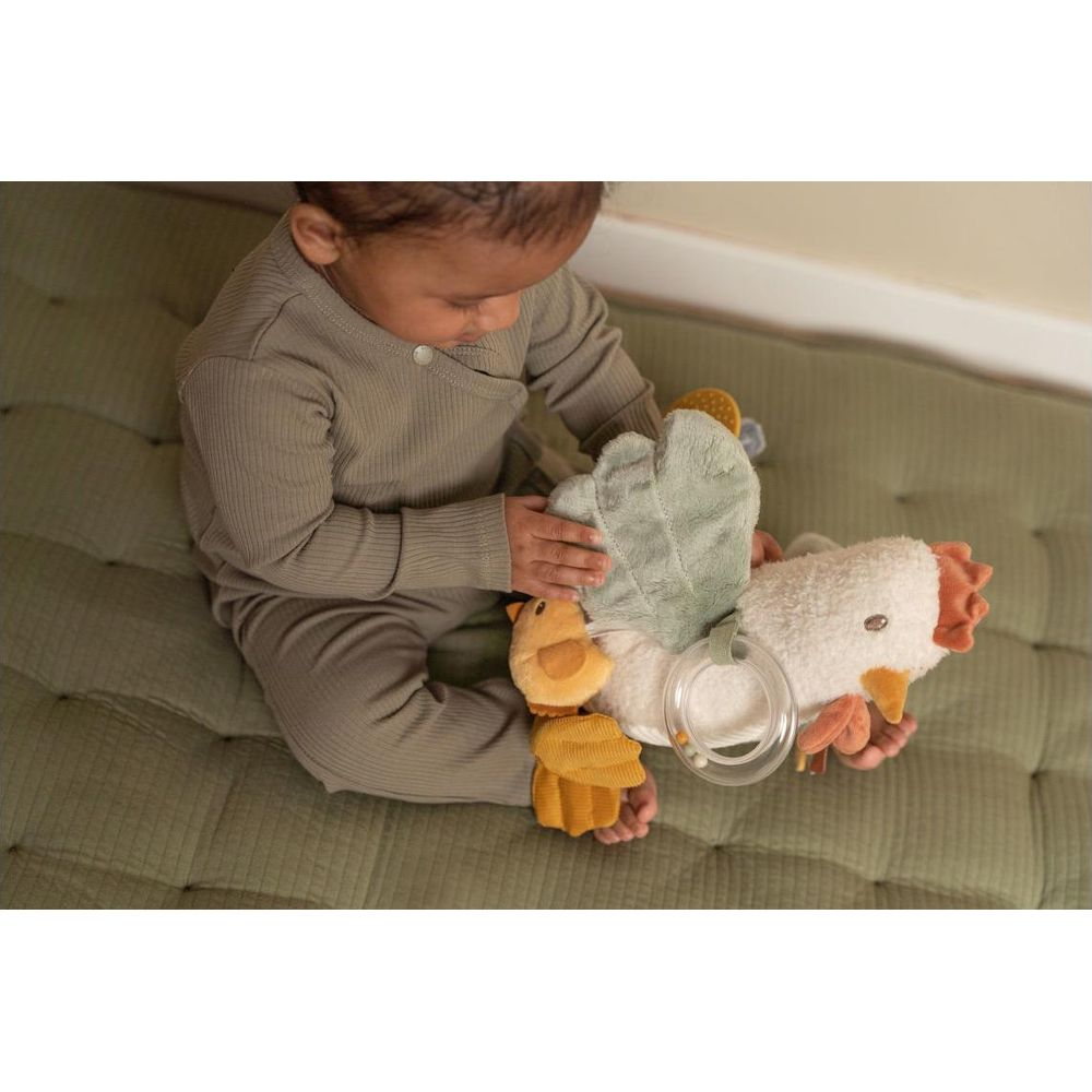 Bébé en tenue vert olive joue avec un jouet poulet doux sur un tapis matelassé vert.