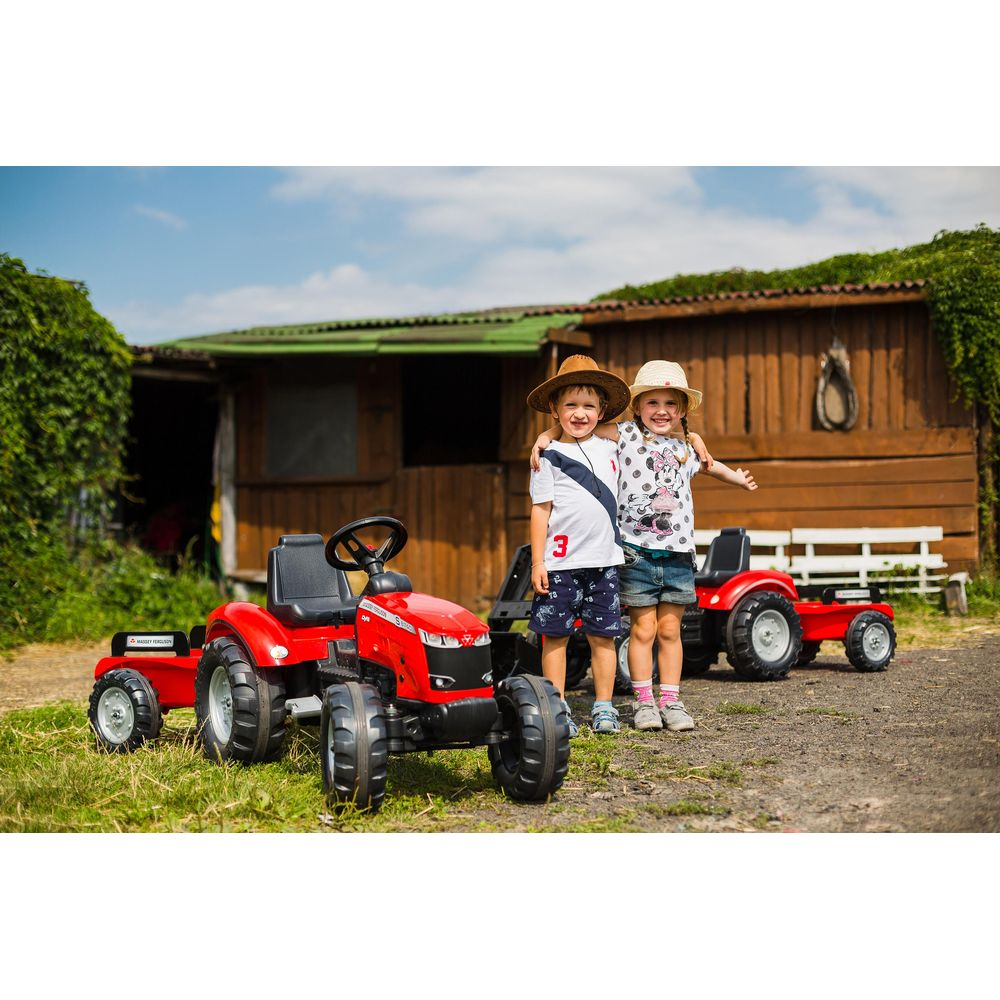 Zwei Kinder stehen zwischen zwei roten Spielzeugtraktoren vor einem Holzschuppen.