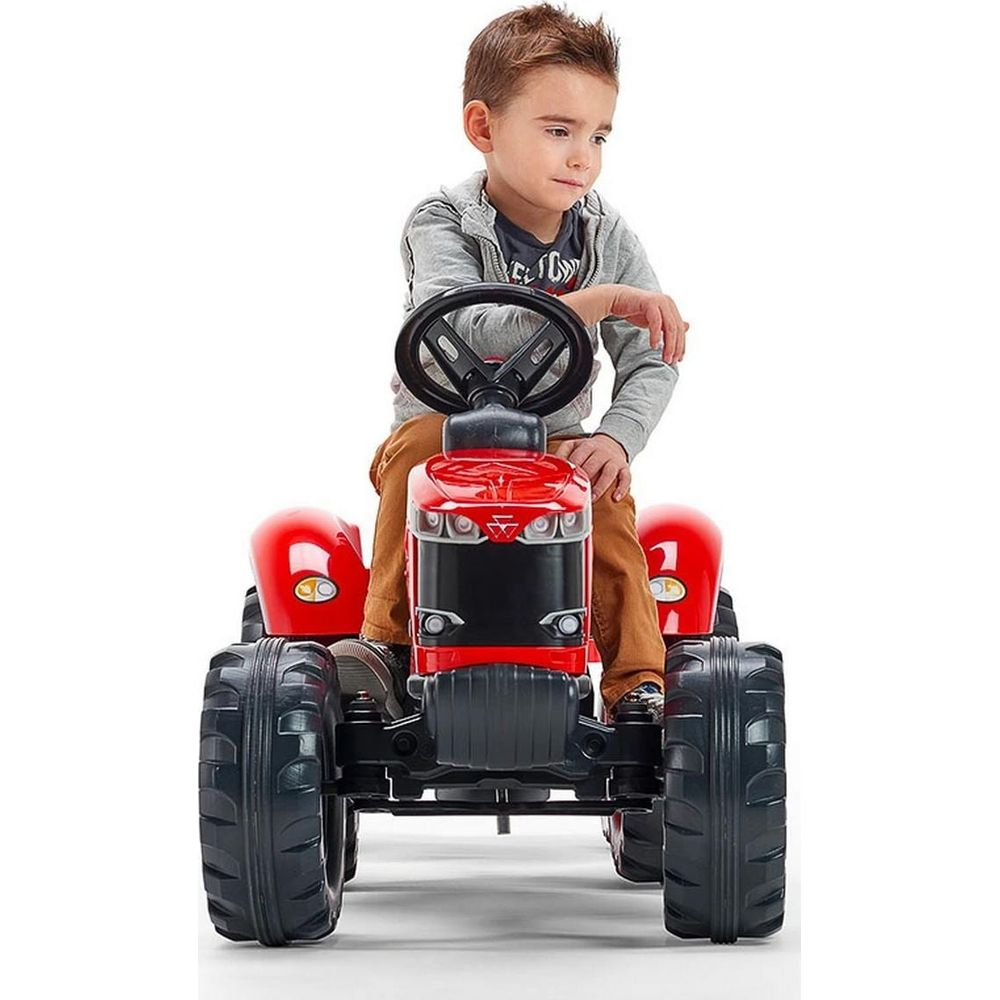 Ein Junge sitzt auf einem roten Spielzeugtraktor mit großen schwarzen Rädern.