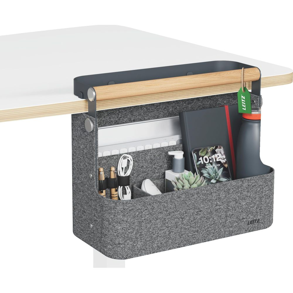 Grauer Filz-Organizer mit Holzgriff, befestigt an einer Schreibtischkante, enthält Stifte, Kabel, Handy, Pflanze, Buch und Flasche.