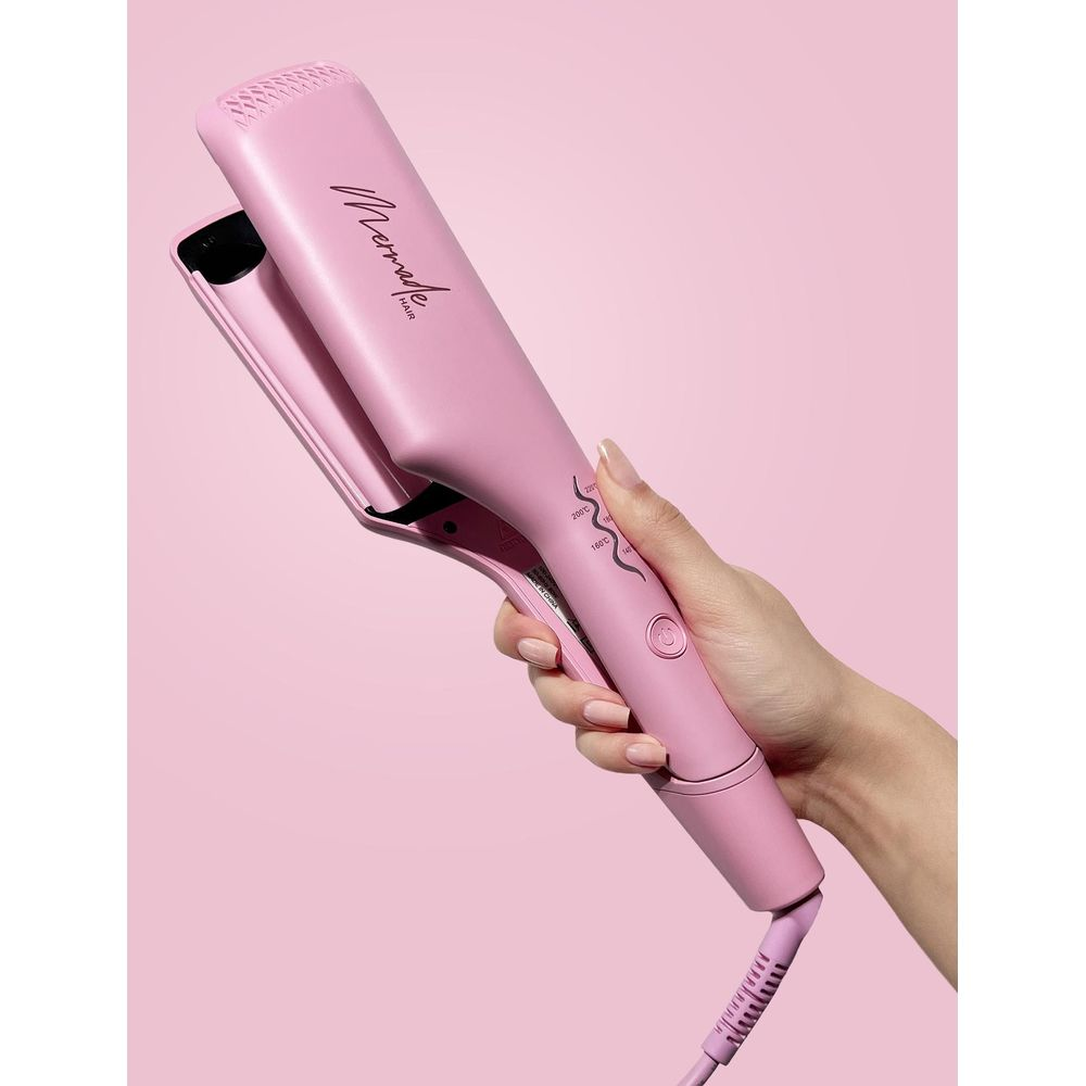 Eine Hand hält einen rosafarbenen Glätteisen mit der Aufschrift „Mermade Hair“.