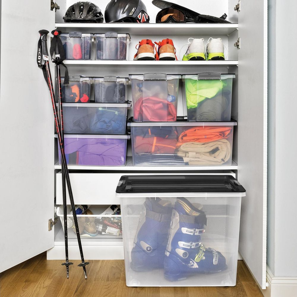Ein Schrank lagert Skiausrüstung: Helme, Brillen, Stiefel, Stöcke, Kleidung in Kisten, Schuhe.