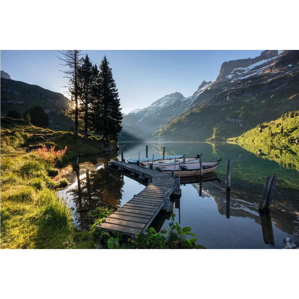 Une jetée en bois mène à des bateaux sur un lac de montagne calme, entouré de pentes vertes.