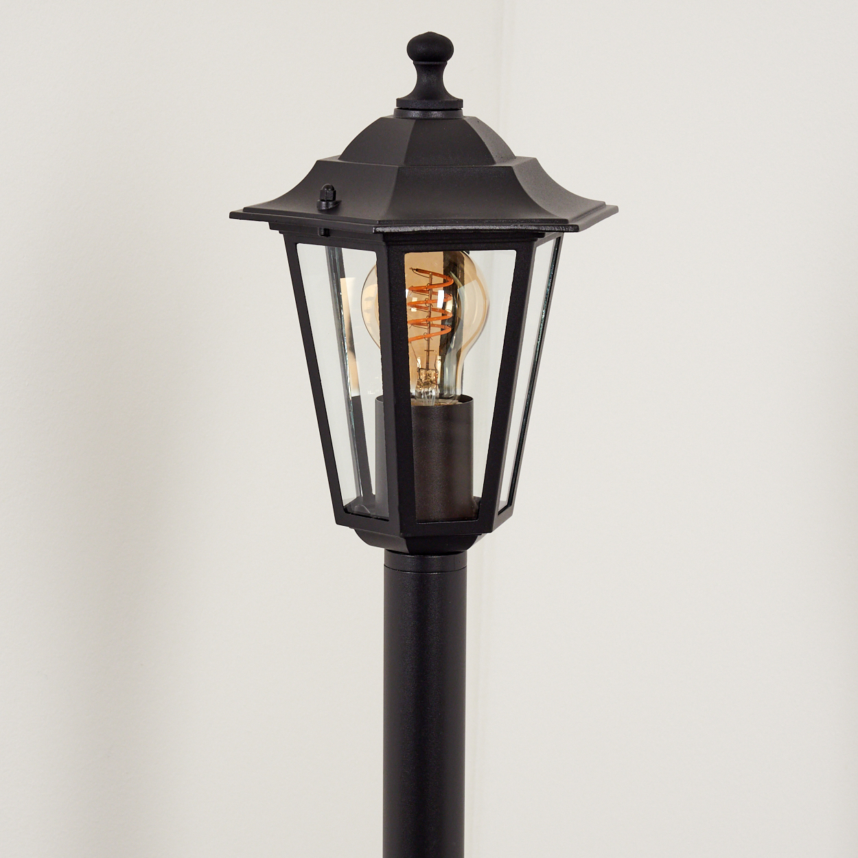 Eine schwarze Laterne mit einem Glühfadenlicht steht vor einem weißen Hintergrund.
