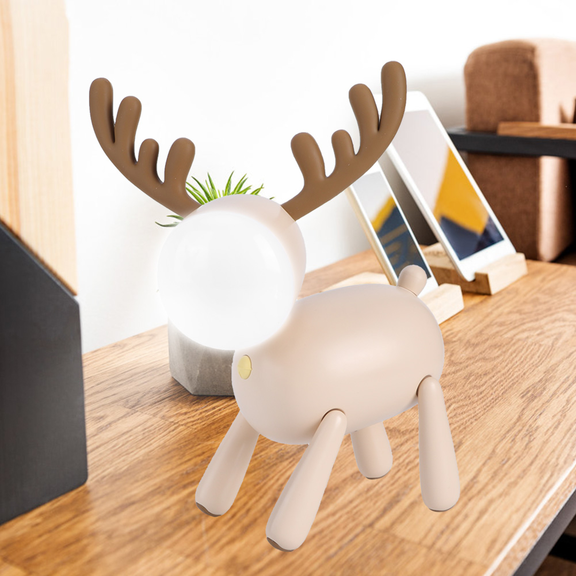 Eine niedliche beige Rentierlampe mit braunen Geweihen steht auf einem Schreibtisch neben Handys.