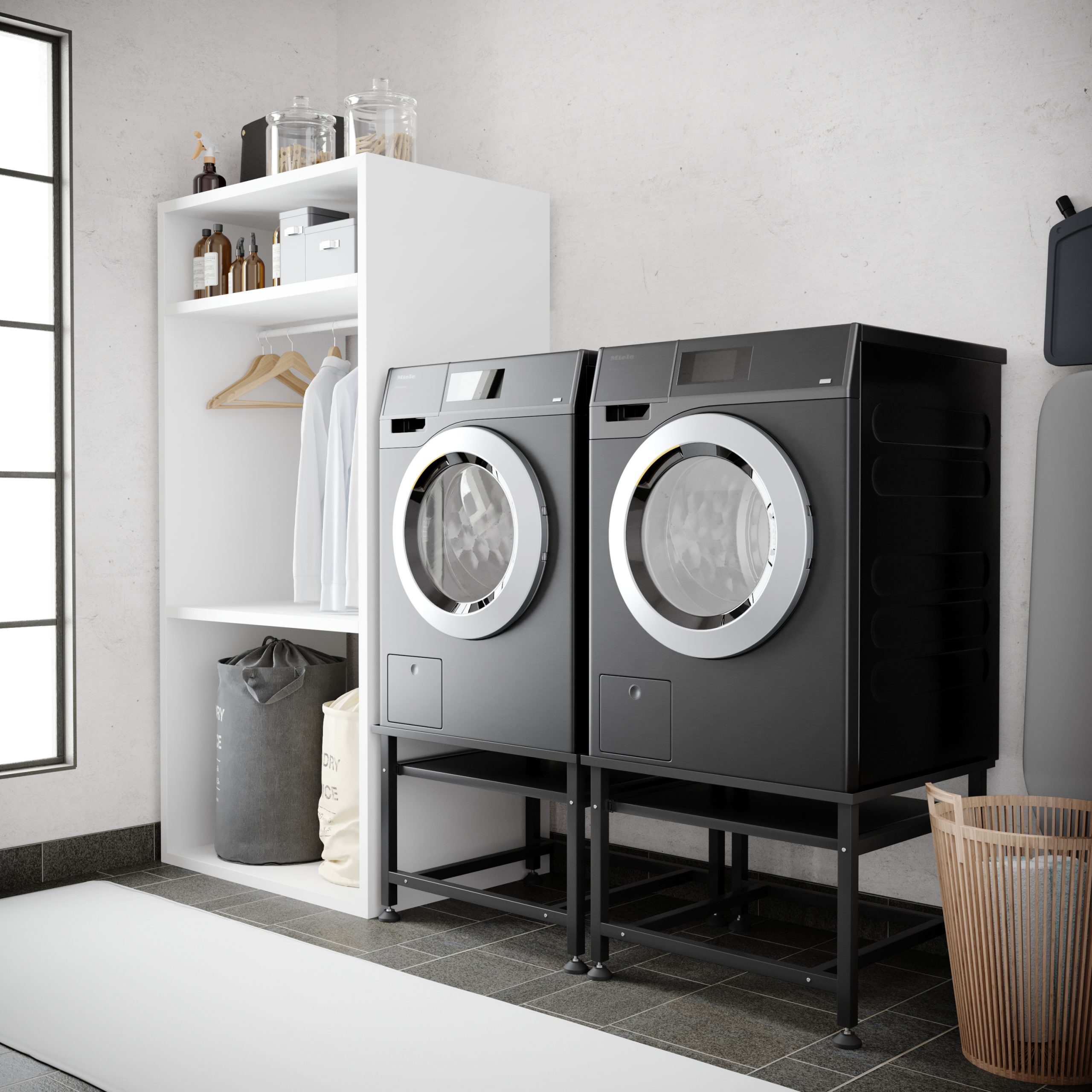 Two black washing machines on stands, next to a shelf with laundry baskets and clothes.
