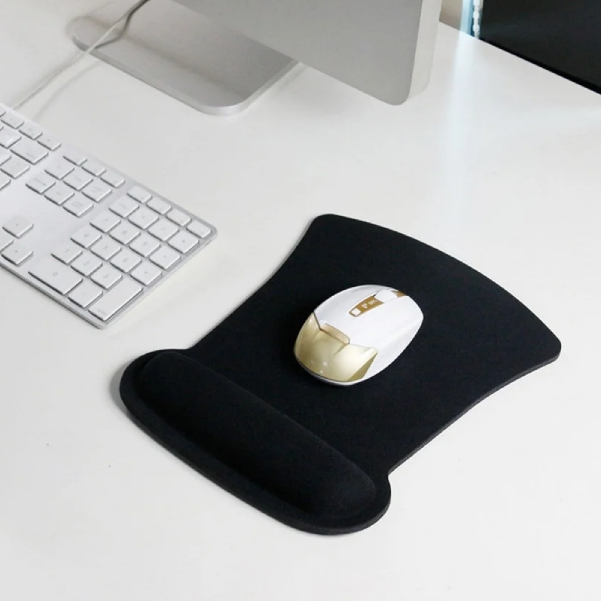 Eine weiße und goldene Computermaus liegt auf einem schwarzen Mauspad neben einer weißen Tastatur.