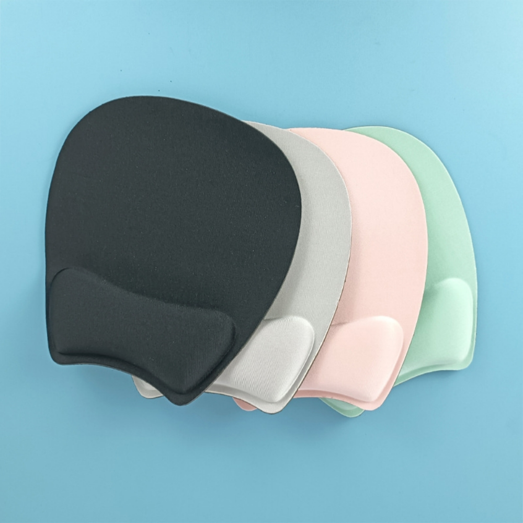 Vier ergonomische Maus-Handgelenkauflagen in Schwarz, Grau, Rosa und Grün auf blauem Hintergrund.