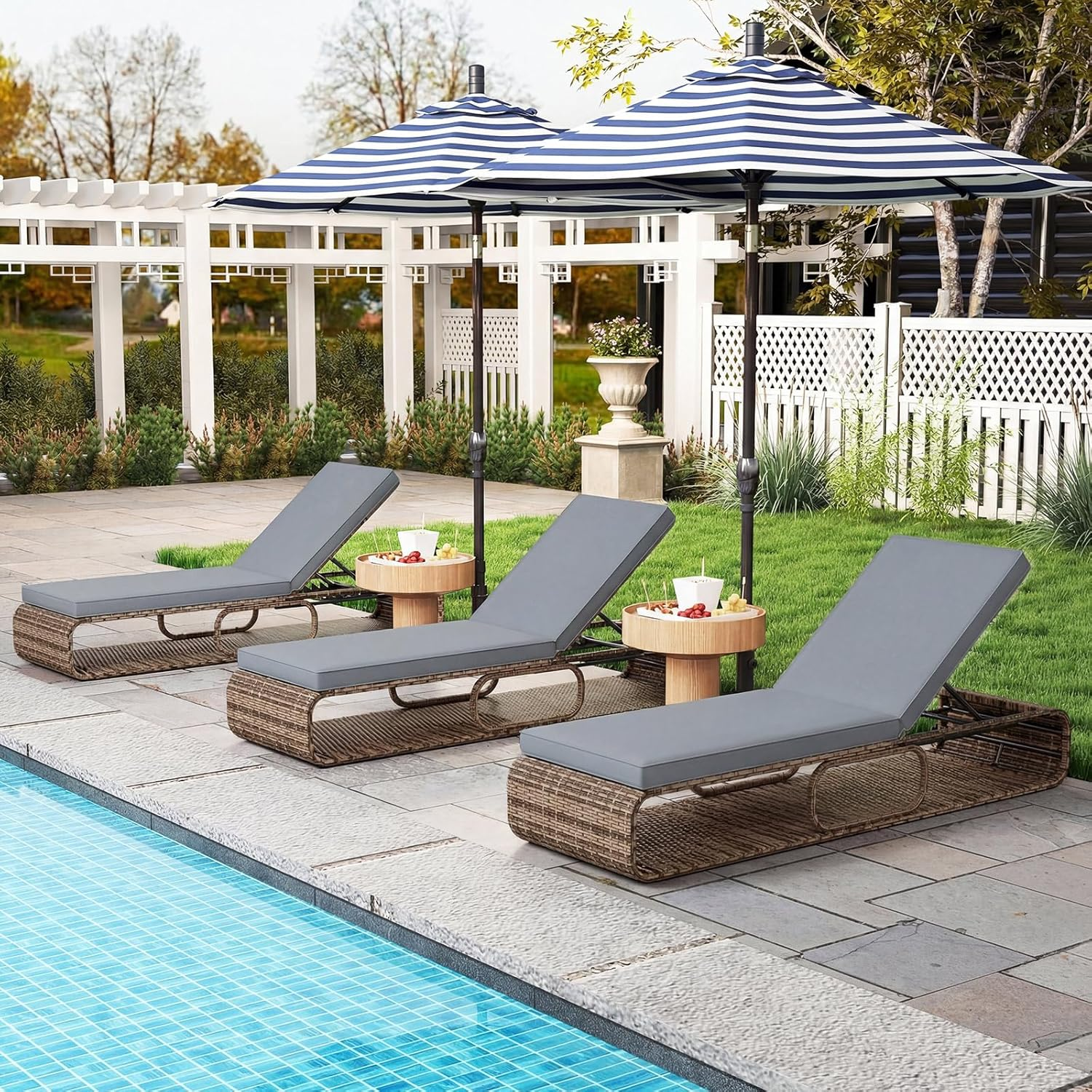Drei Liegen mit grauen Polstern neben einem Pool unter blau-weißen gestreiften Sonnenschirmen.
