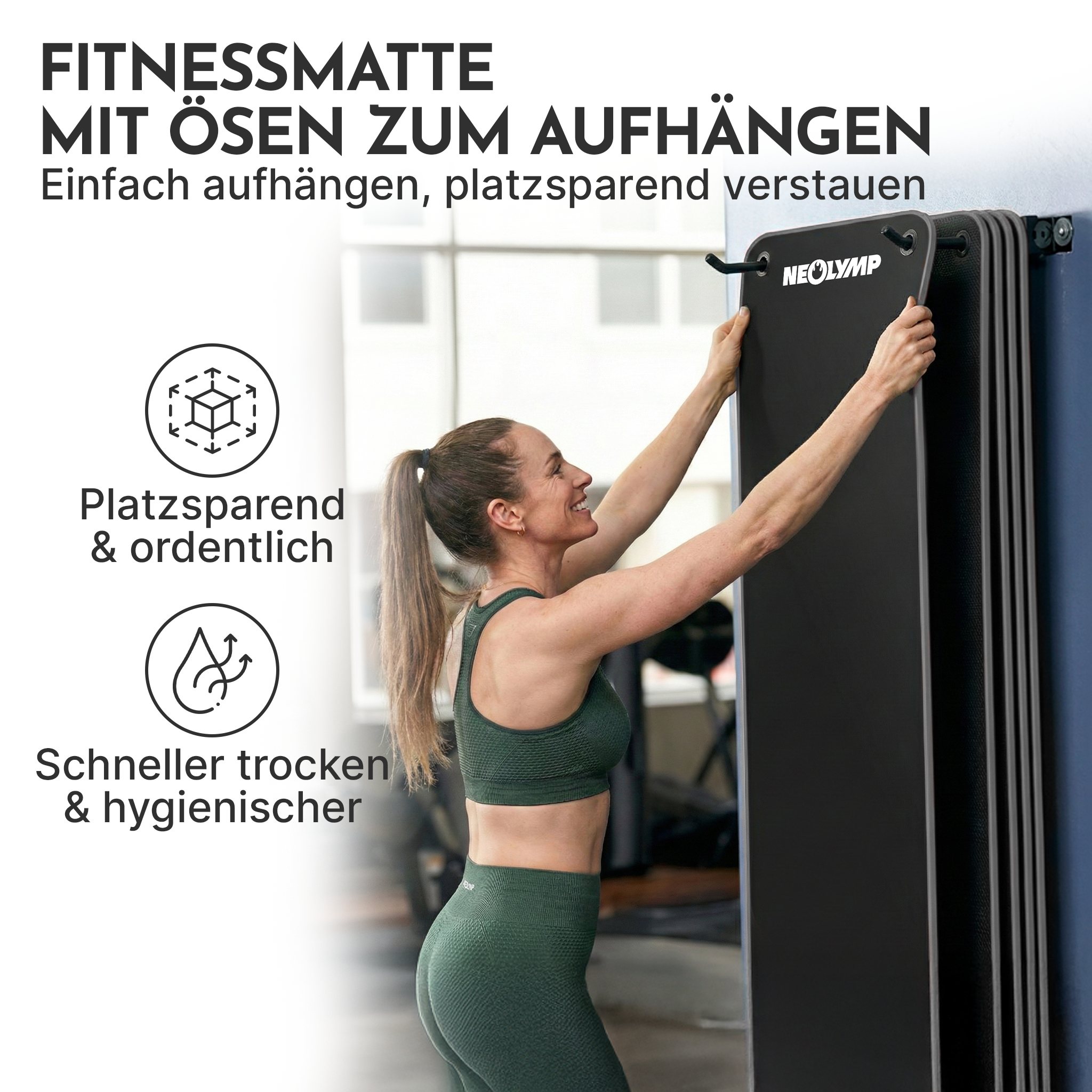 Eine Frau hängt eine schwarze Fitnessmatte mit Ösen an die Wand.