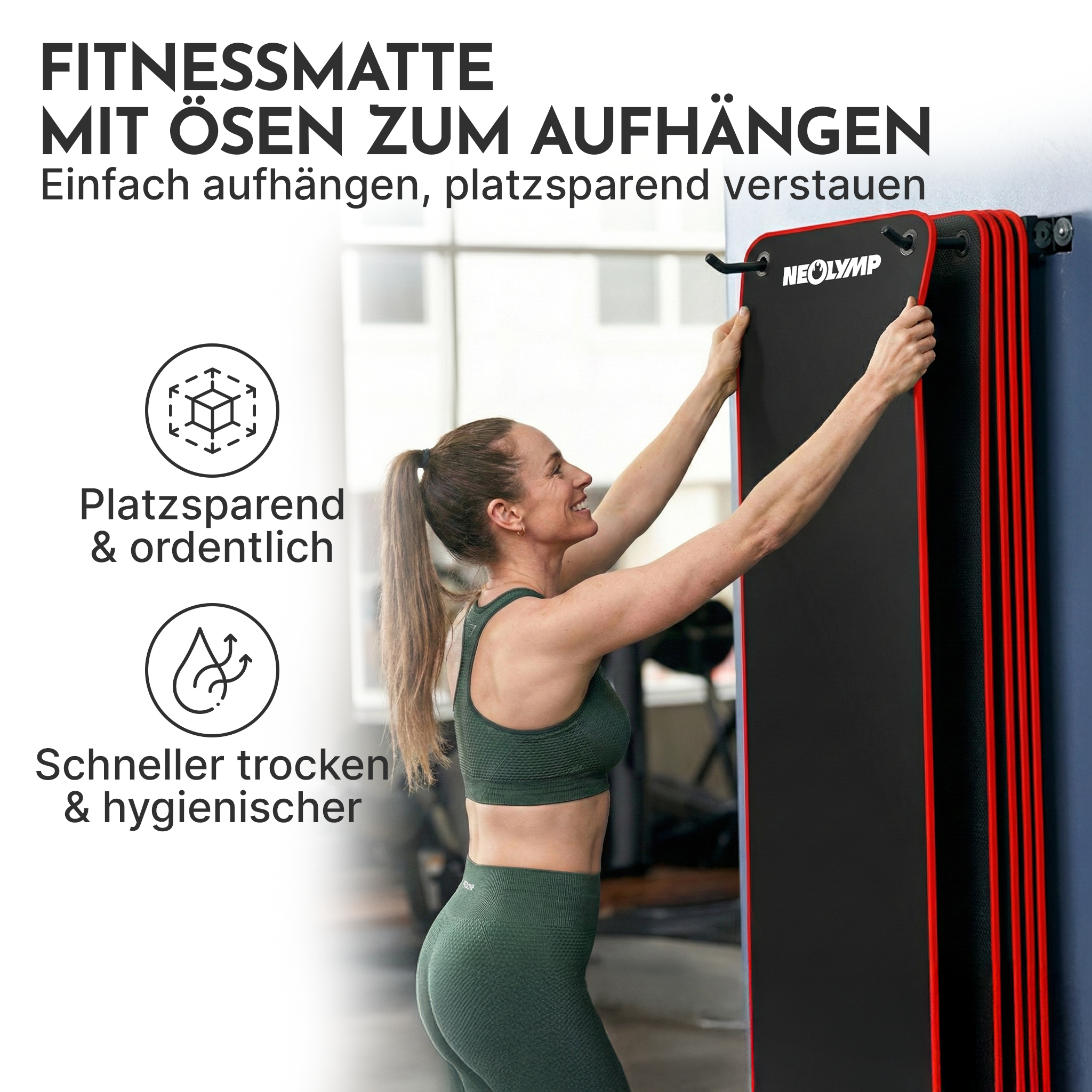 Eine Frau hängt eine schwarze Fitnessmatte mit roten Kanten an die Wand.