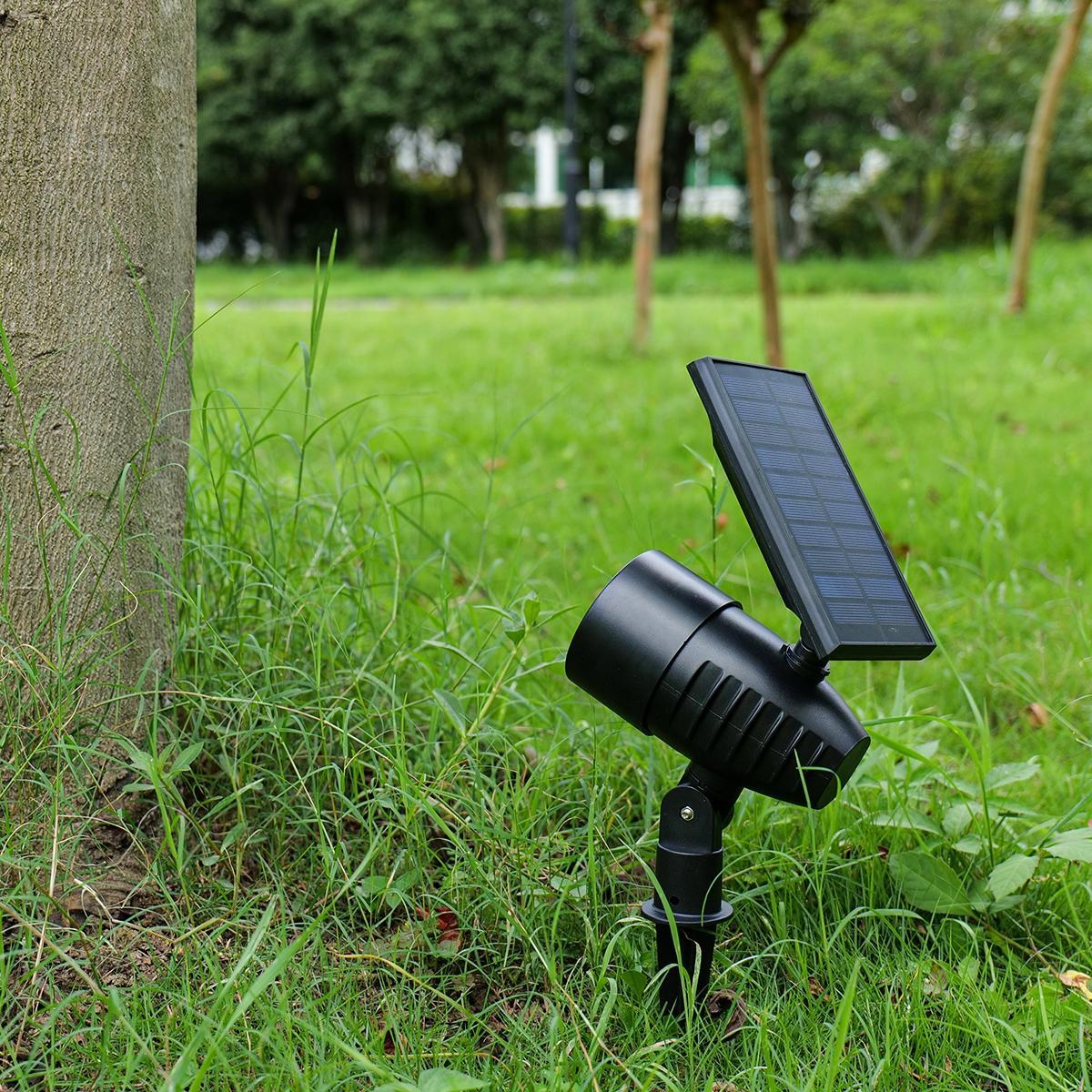Schwarzer Solarstrahler mit Panel im Gras neben einem Baum.