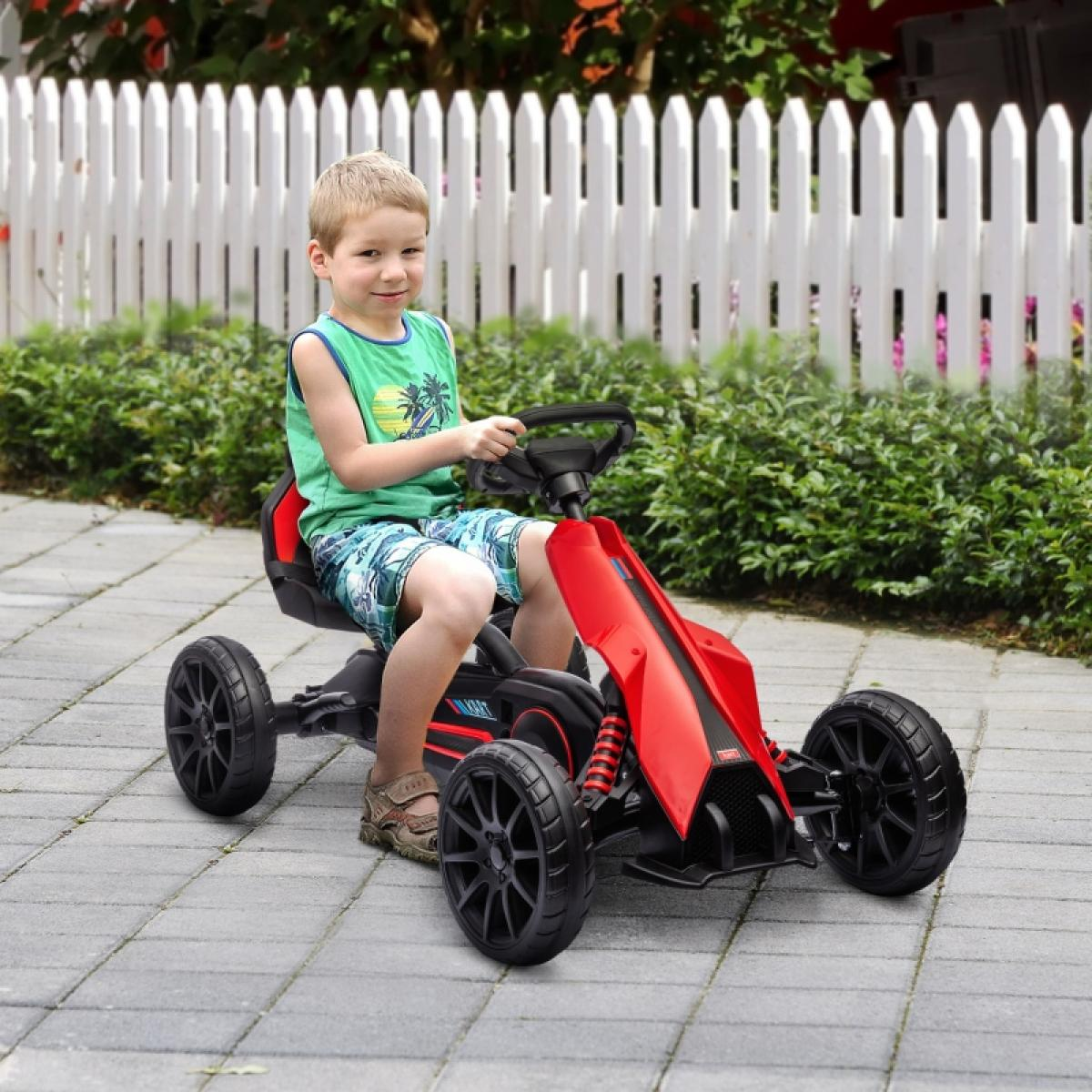 Ein Junge fährt ein rotes Go-Kart auf einer gepflasterten Auffahrt mit einem weißen Zaun im Hintergrund.
