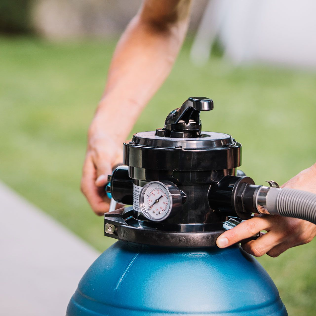 Eine Person stellt einen blauen Poolfilter ein. Ein Manometer ist sichtbar.