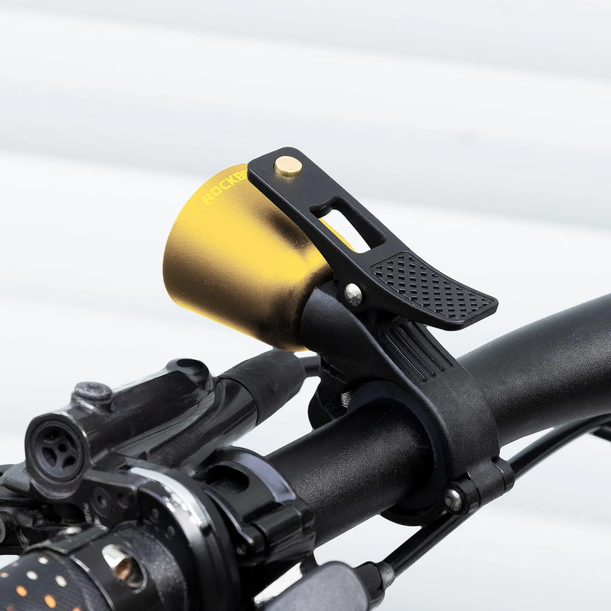 Goldene Fahrradklingel mit schwarzem Halter an einem Lenker.