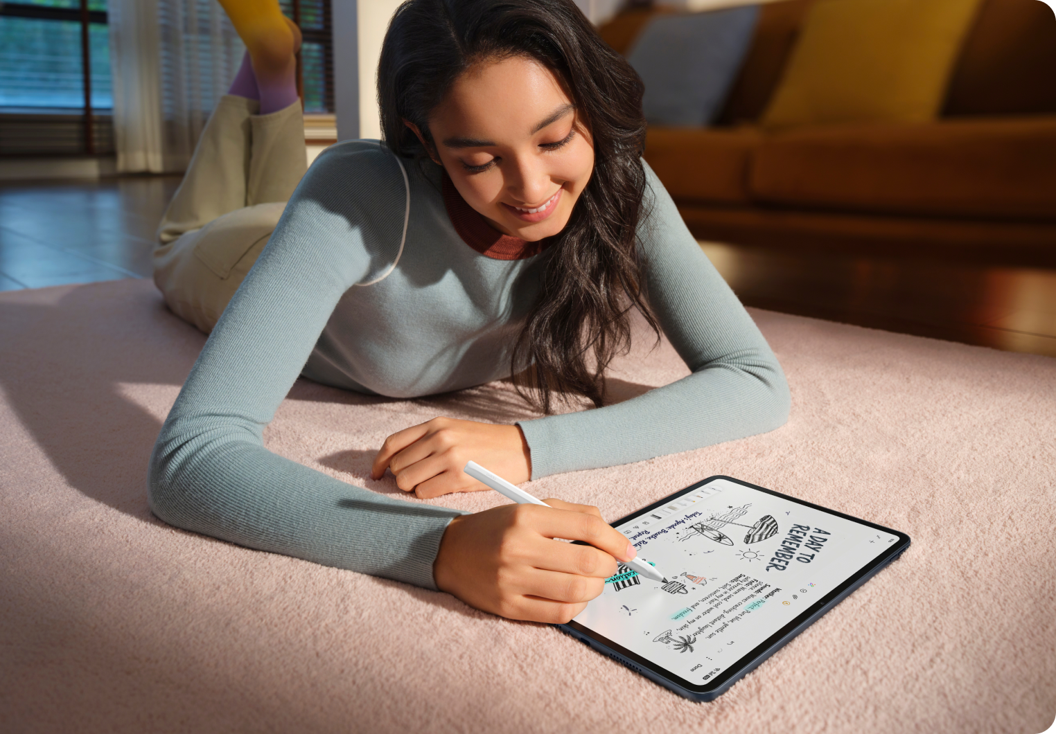 Eine junge Frau liegt auf einem rosa Teppich und zeichnet mit einem Stift auf einem Tablet. Sie trägt ein blaues Oberteil.