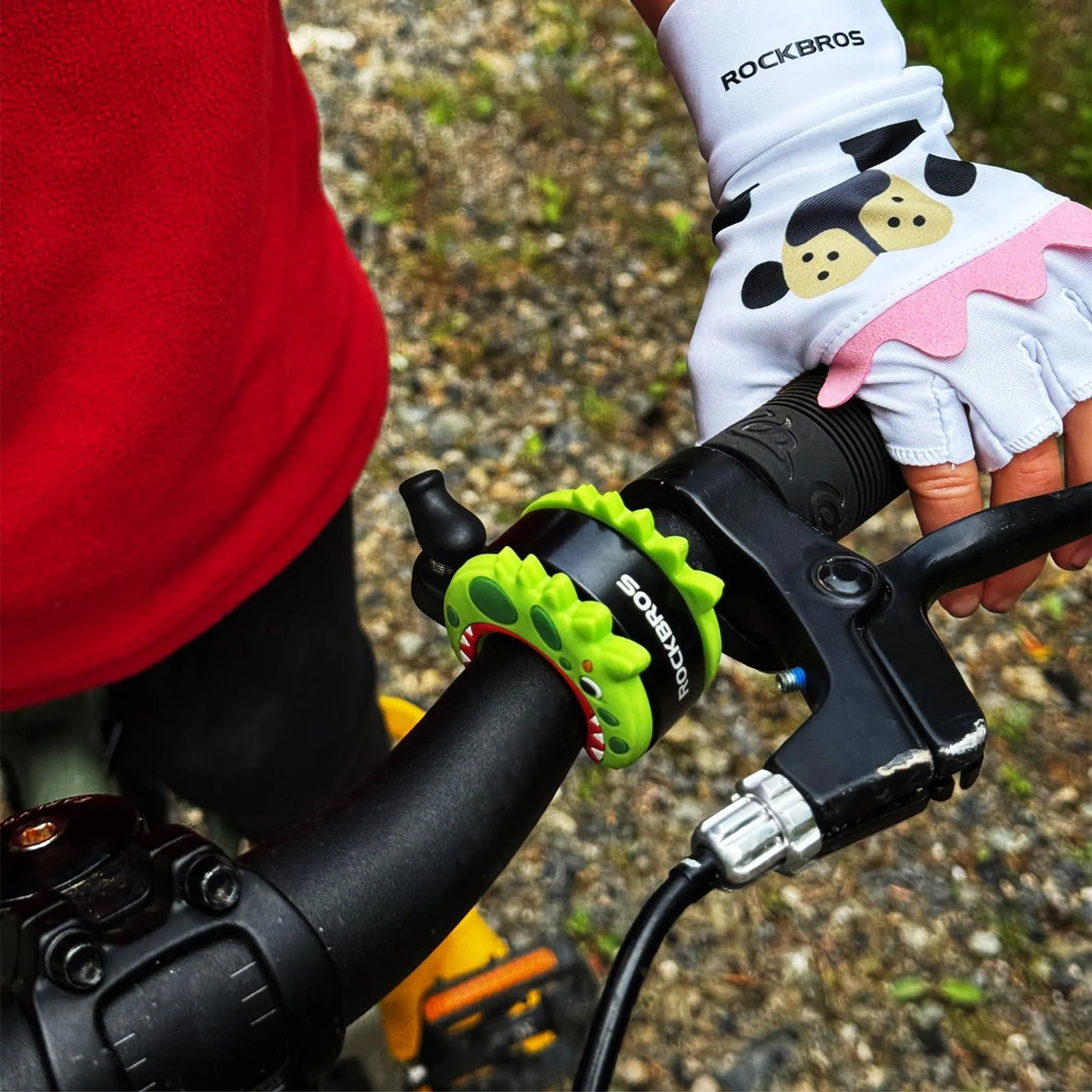 Kind hält Fahrradlenker mit grünem Dino-Ring und Kuh-Handschuh.