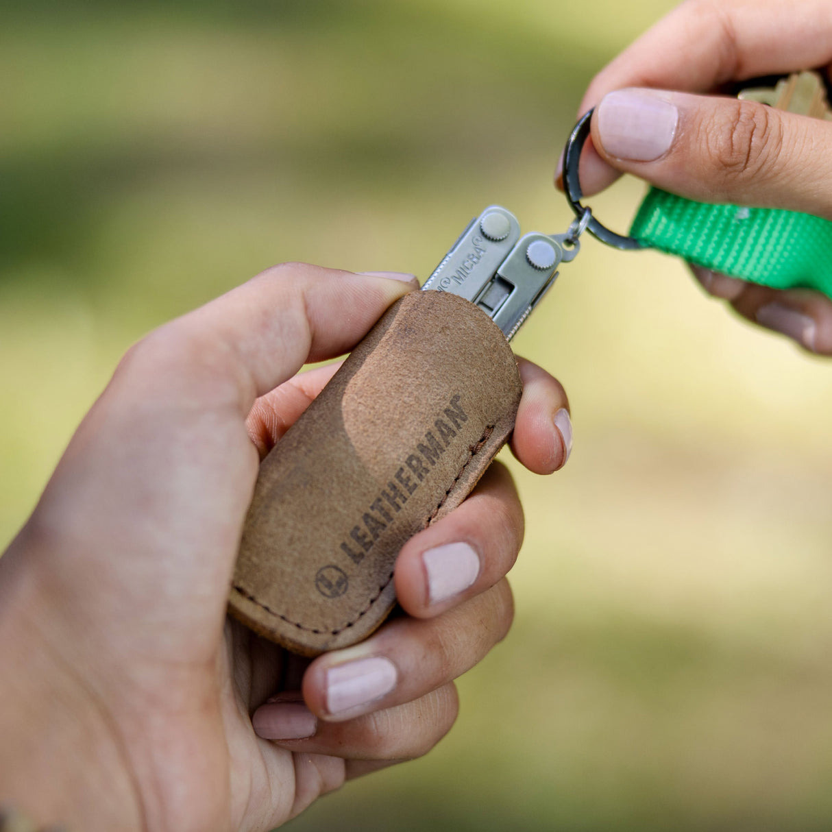 Hände halten einen braunen Leatherman-Etui mit einem Multitool und Schlüsselring.