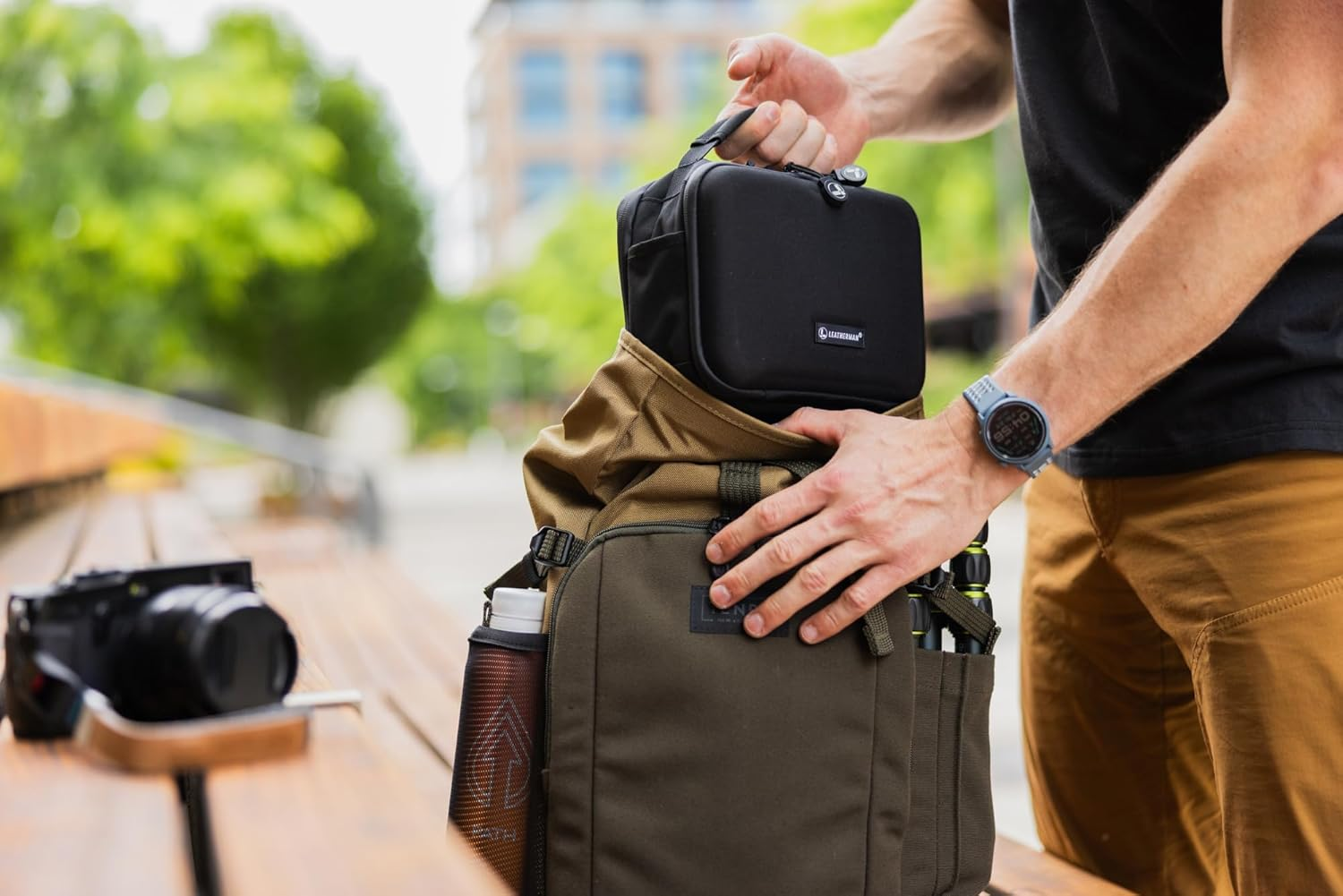 Mann packt schwarze Tasche in Rucksack. Kamera liegt daneben.