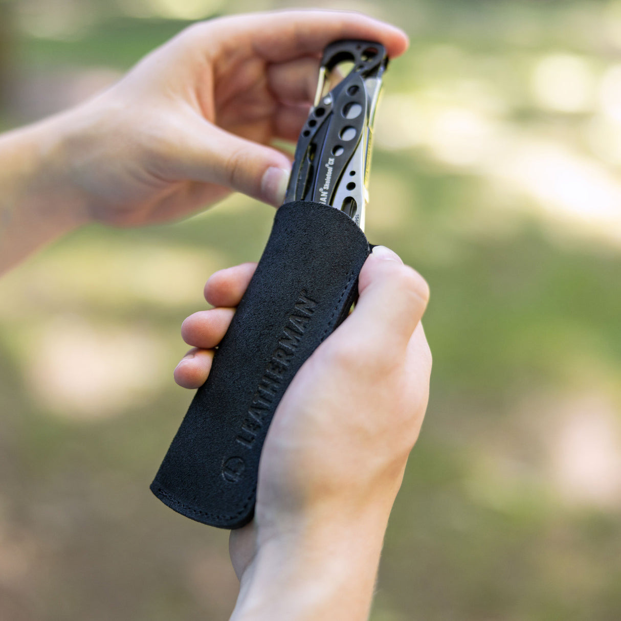 Hände stecken ein schwarzes Multitool in eine schwarze Hülle mit Leatherman-Logo.