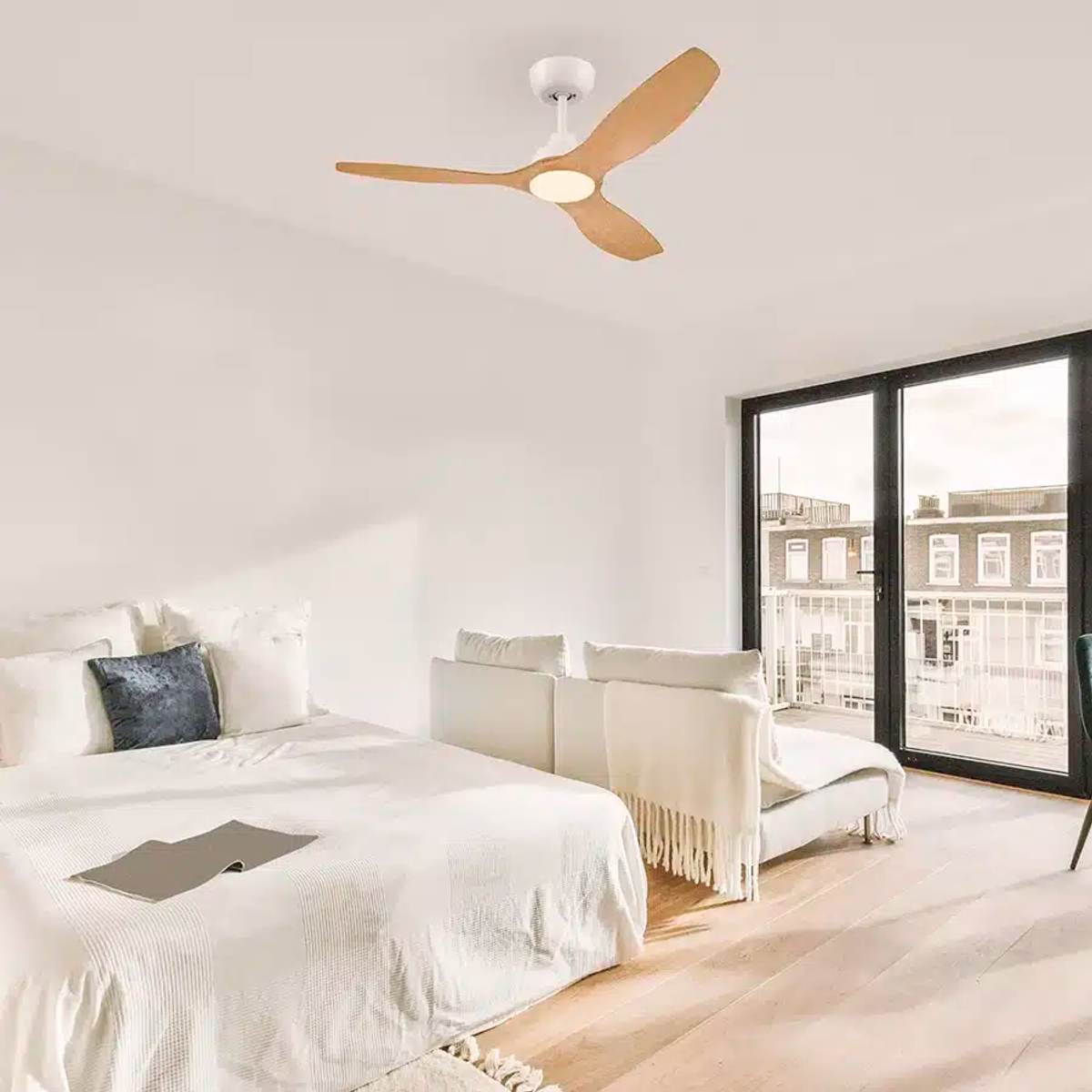 Un dormitorio moderno con cama blanca, sofá blanco y ventilador de techo de madera.