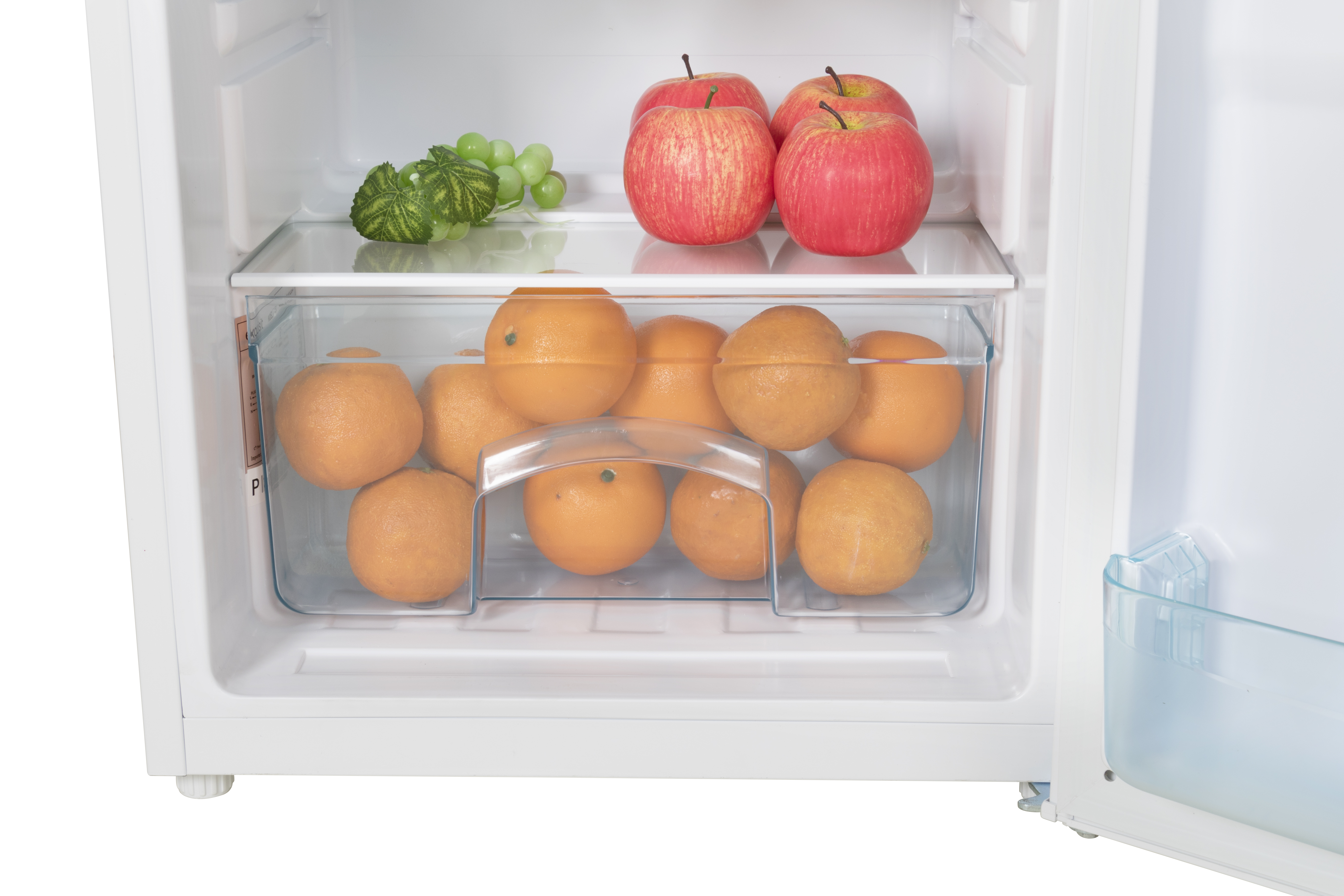Inside a white refrigerator: red apples on top shelf, oranges in drawer, and green grapes.